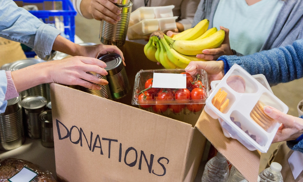 people gathered around a box marked "donations" with food and cans to donate