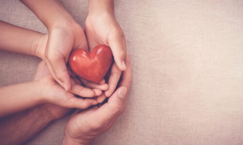 three pairs of hands holding a wooden heart